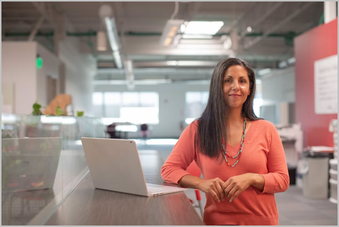 Professional standing beside a laptop in a modern office